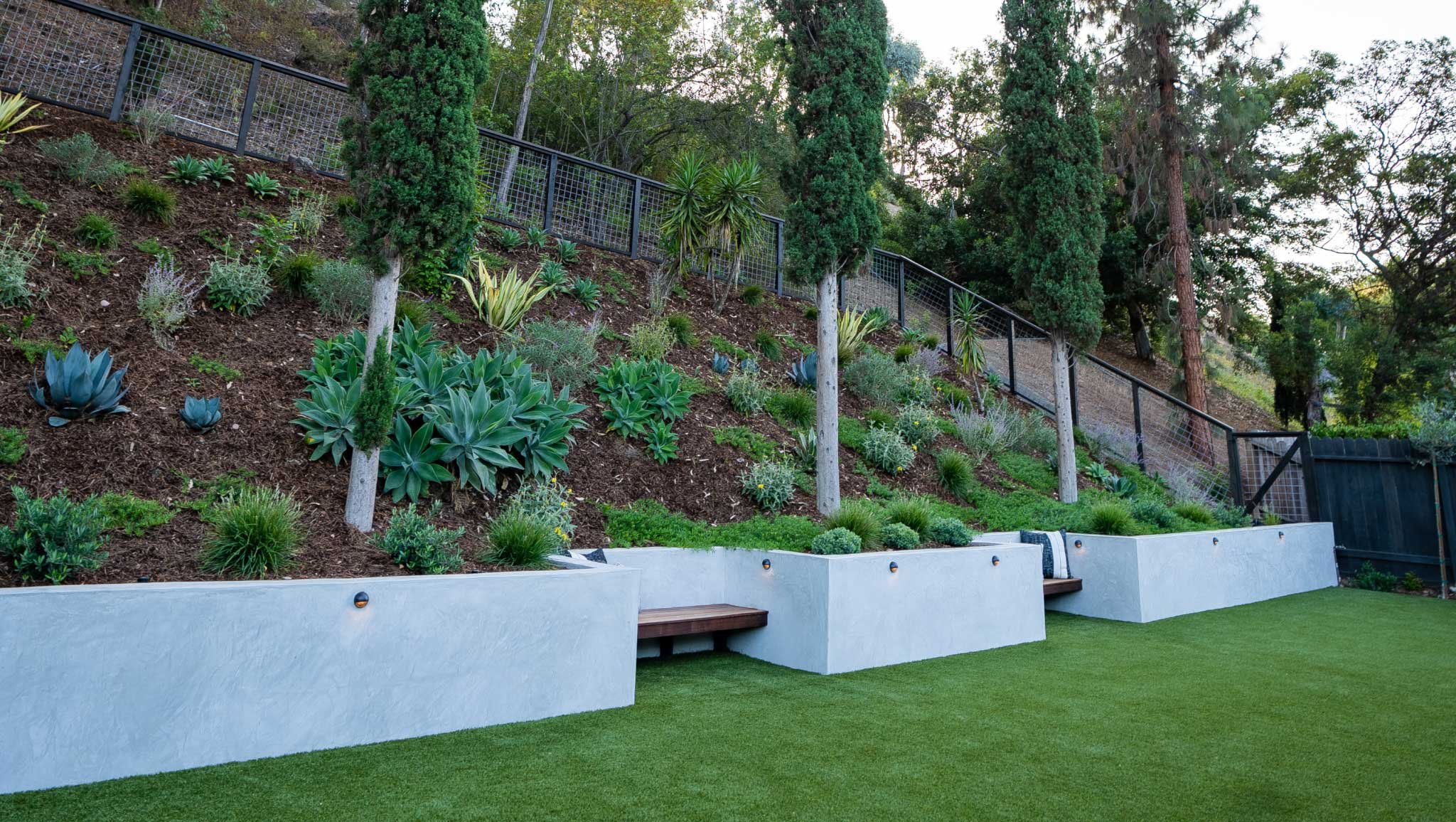 院子的斜坡部分有现代挡土墙，斜坡上有内置的长凳和植物