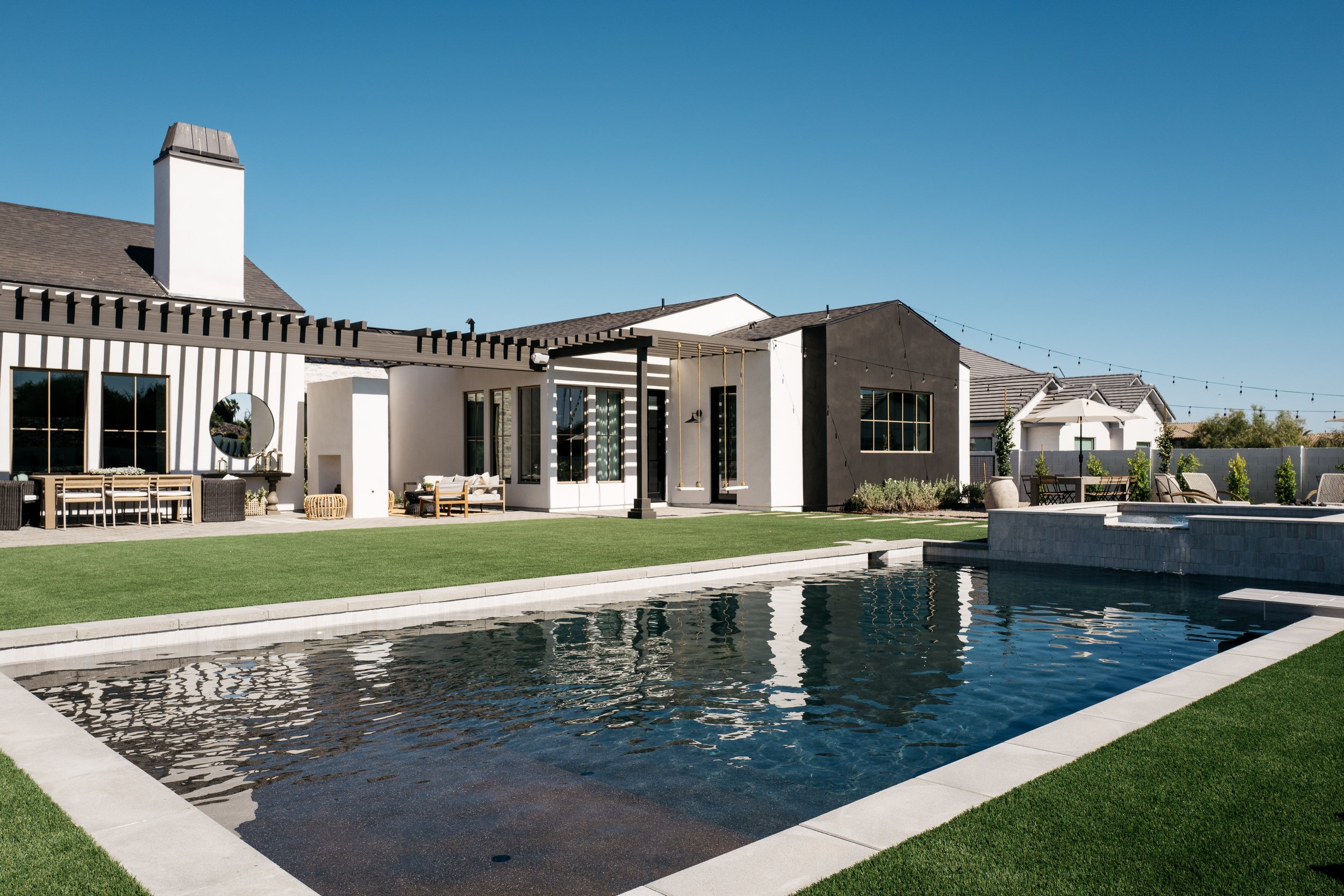 现代后院的角度视图，带有大游泳池，草坪和定制的黑色凉棚，延伸到家庭外部