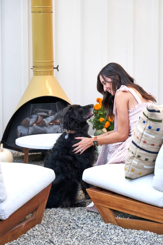 克里斯蒂和她的狗狗坐在户外躺椅上，旁边是他们世纪中叶的现代户外壁炉