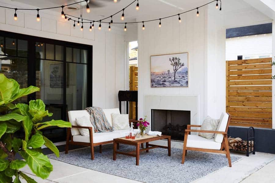 覆盖户外起居室和壁炉上面用绳子灯,otudoor沙发,咖啡桌,蓝色与白色躺椅垫在户外地毯,和小提琴叶在前景图